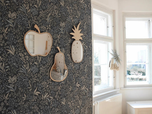 Apple-shaped wooden mirror with acrylic glass displayed on dark floral wallpaper next to pear and pineapple mirrors