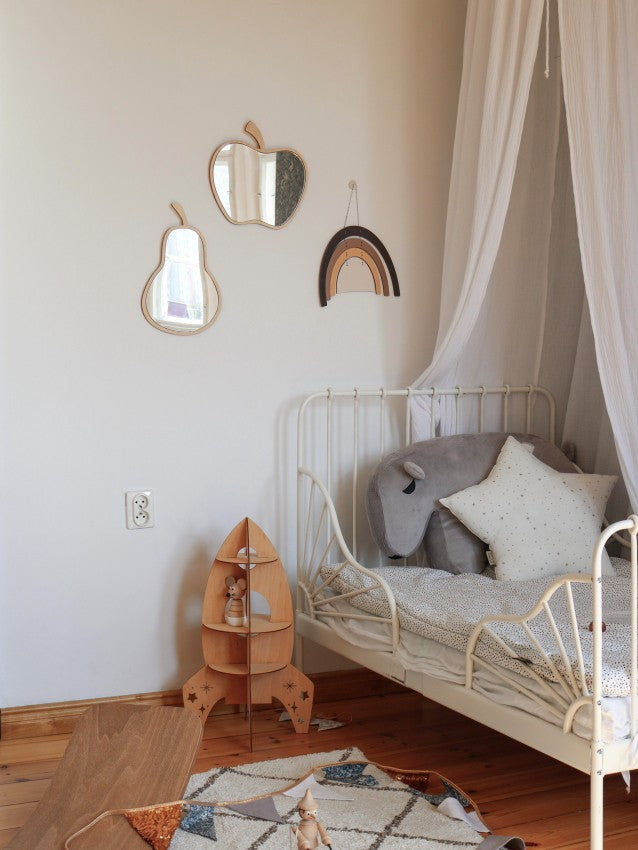 Apple wood mirror hung above white metal crib in light nursery with pear mirror and rainbow wall decor