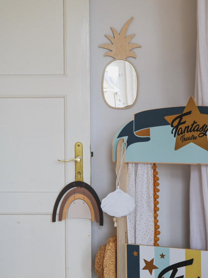 Pineapple-shaped mirror with natural wood frame hung on nursery wall above storage basket