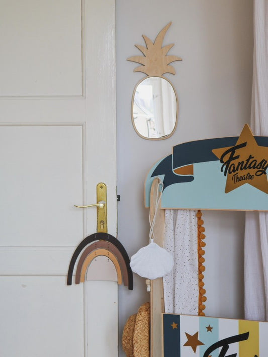 Pineapple-shaped mirror with natural wood frame hung on nursery wall above storage basket