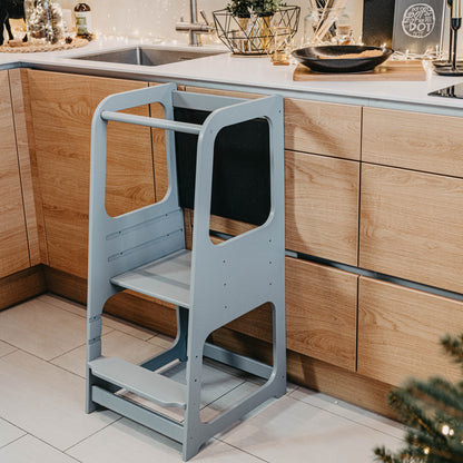 Light blue Montessori kitchen tower with blackboard beside wooden cabinetry