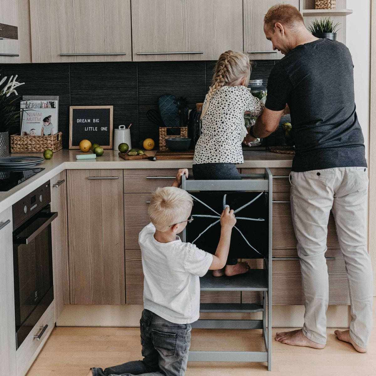 Children using black kitchen tower with blackboard panel to help at adult counter height