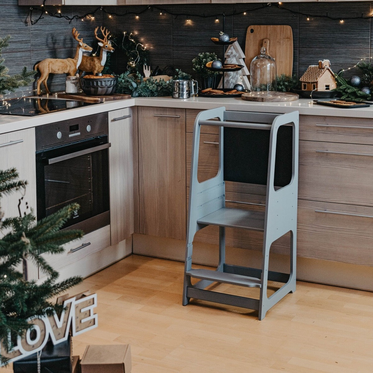 Light blue wooden Montessori kitchen helper tower standing in modern kitchen with holiday decor