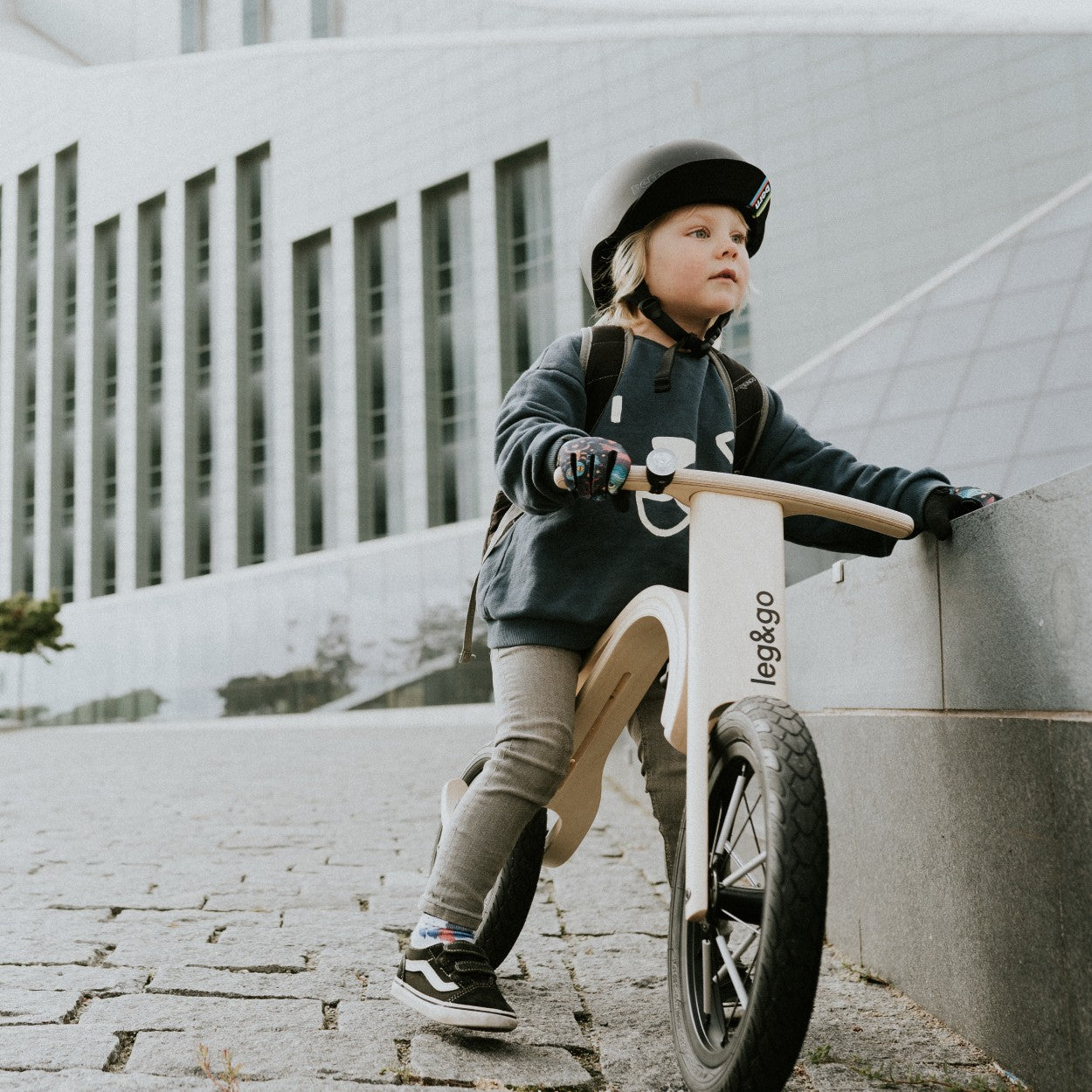 Child with black helmet leaning on leg&go wooden balance bike 3in1 – cool urban kids bike moment