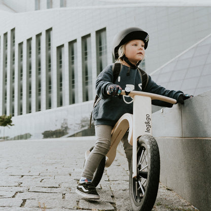 Child with black helmet leaning on leg&go wooden balance bike 3in1 – cool urban kids bike moment