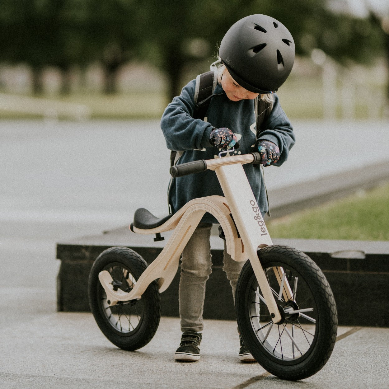 Child in black helmet with leg&go wooden balance bike 3in1 – urban outdoor kids bike setting