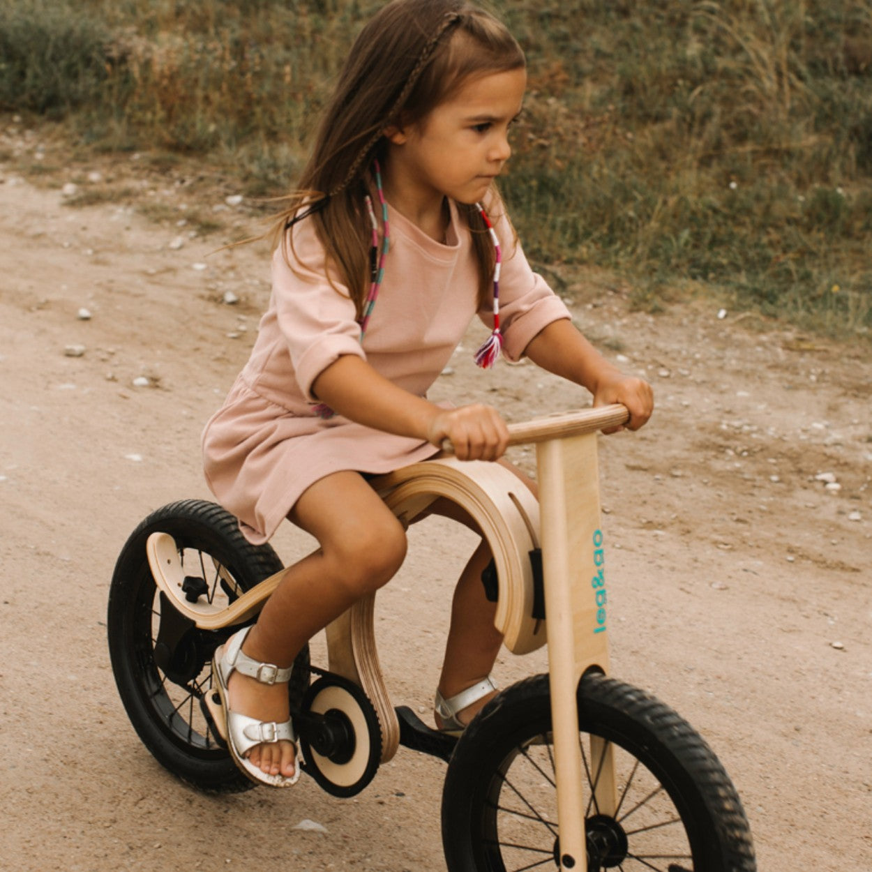Child riding wooden leg&go balance bike with pedals on dirt path