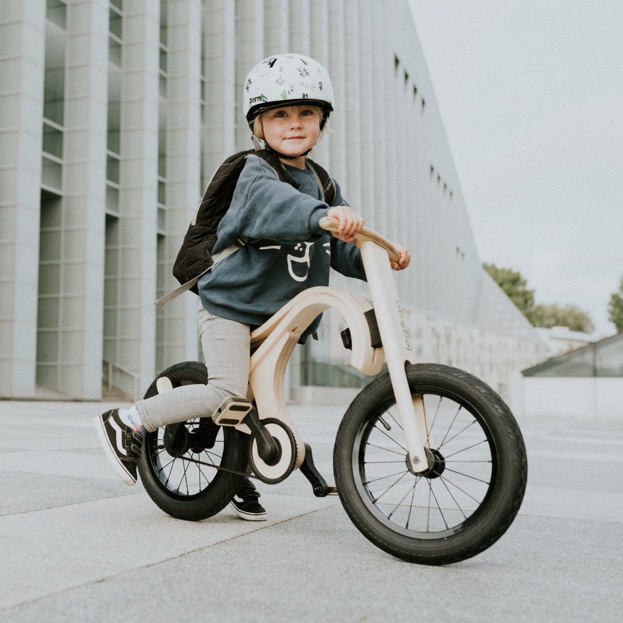 Child in helmet riding white and natural wood leg&go pedal bike outdoors