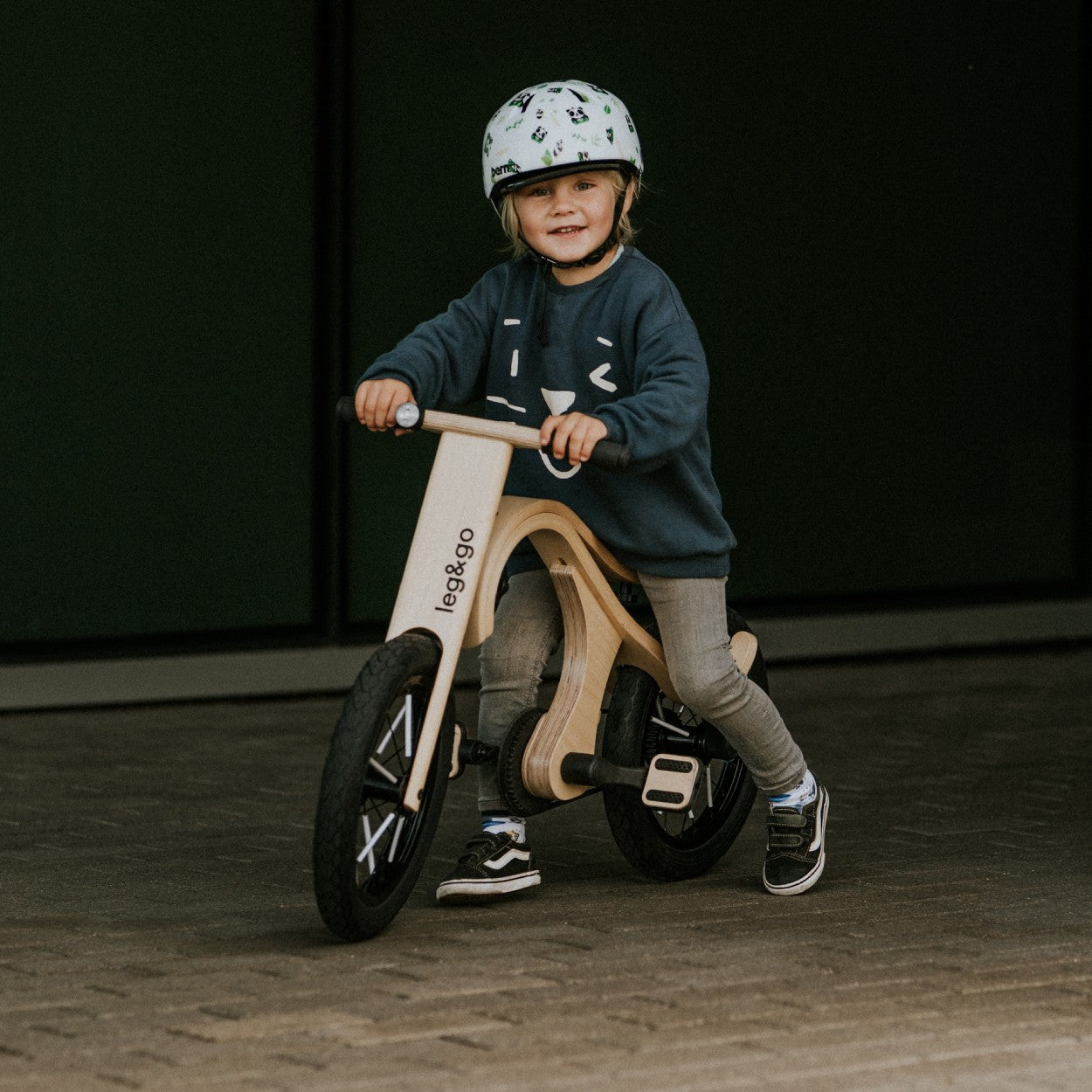Young child holding handlebar of wooden leg&go bike with pedals