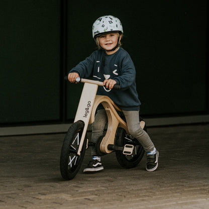 Young child holding handlebar of wooden leg&go bike with pedals