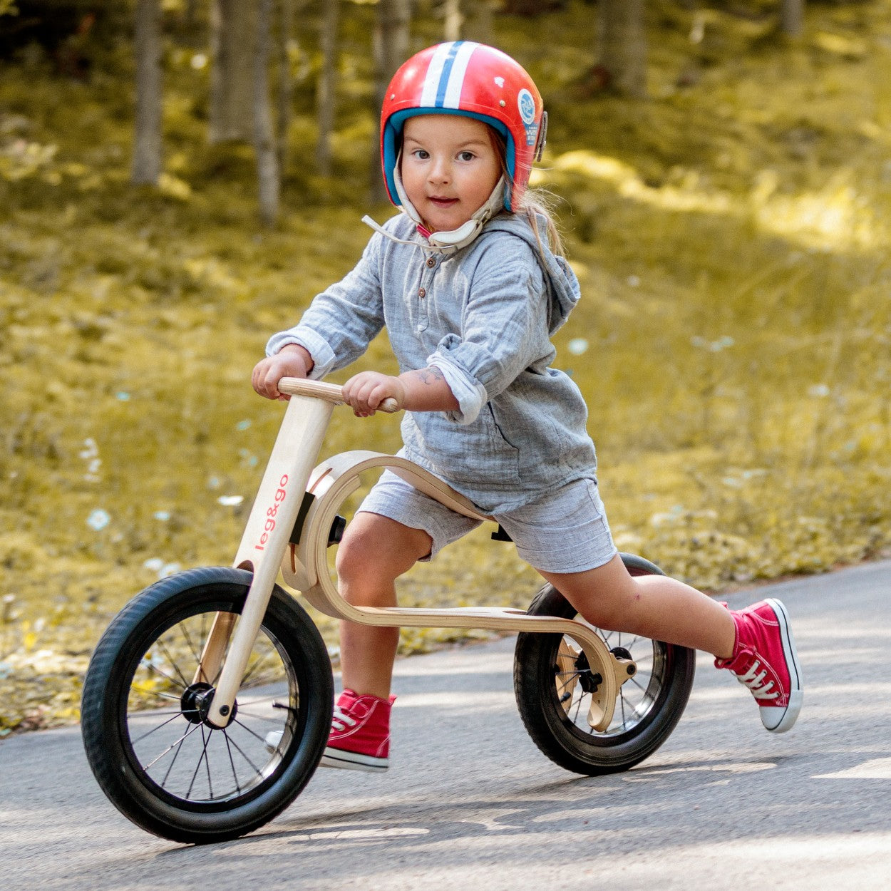 Smiling girl with red helmet riding leg&go 3in1 wooden balance bike – fun outdoor toddler ride