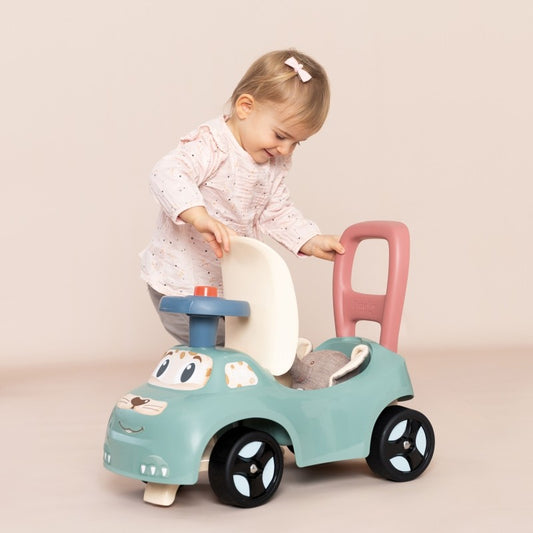 Toddler sitting on turquoise ride-on pusher with pink handle and horn, demonstrating seated play