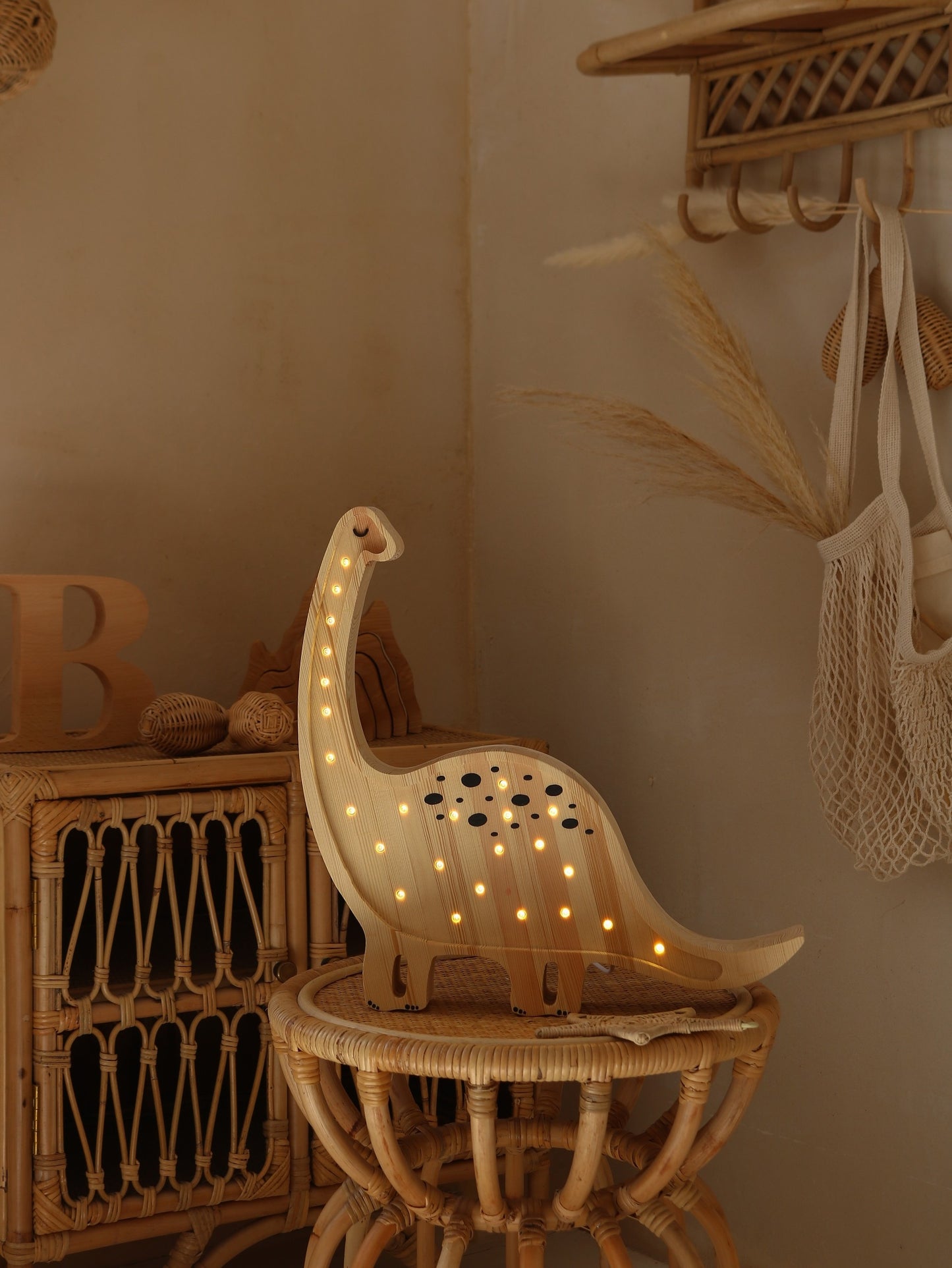 Natural wood diplodocus lamp with warm white LED lights glowing on neck and body, displayed on woven side table in styled