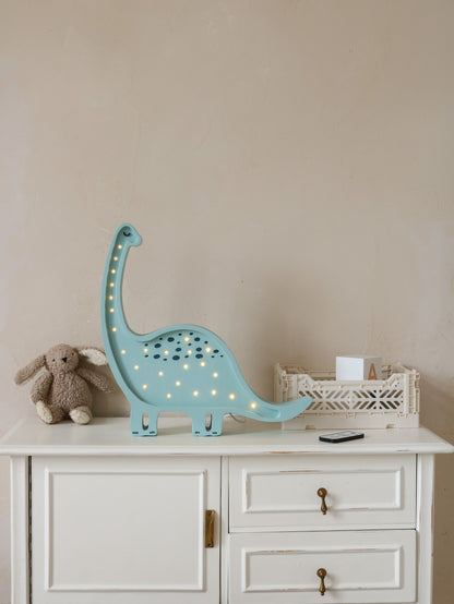 Light blue diplodocus children's lamp with warm LED lights on white dresser beside stuffed rabbit toy