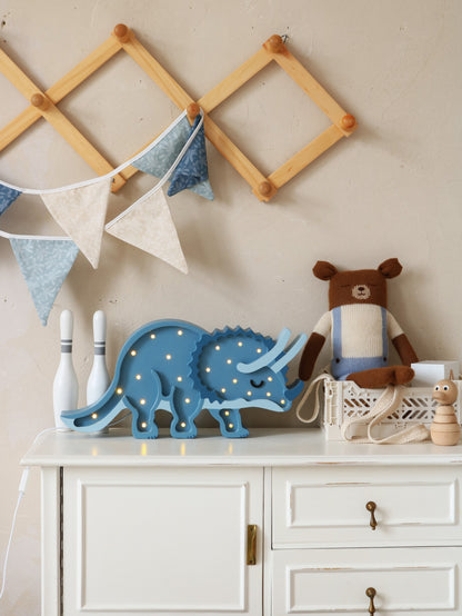 Blue triceratops dinosaur lamp styled on a white dresser in a nursery setting