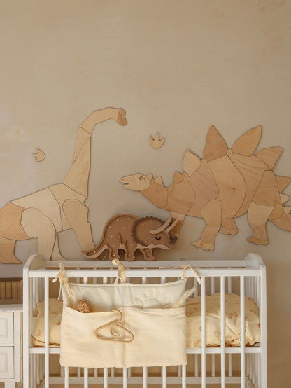 Beige dinosaur wall decals with natural wood triceratops lamp above a baby crib