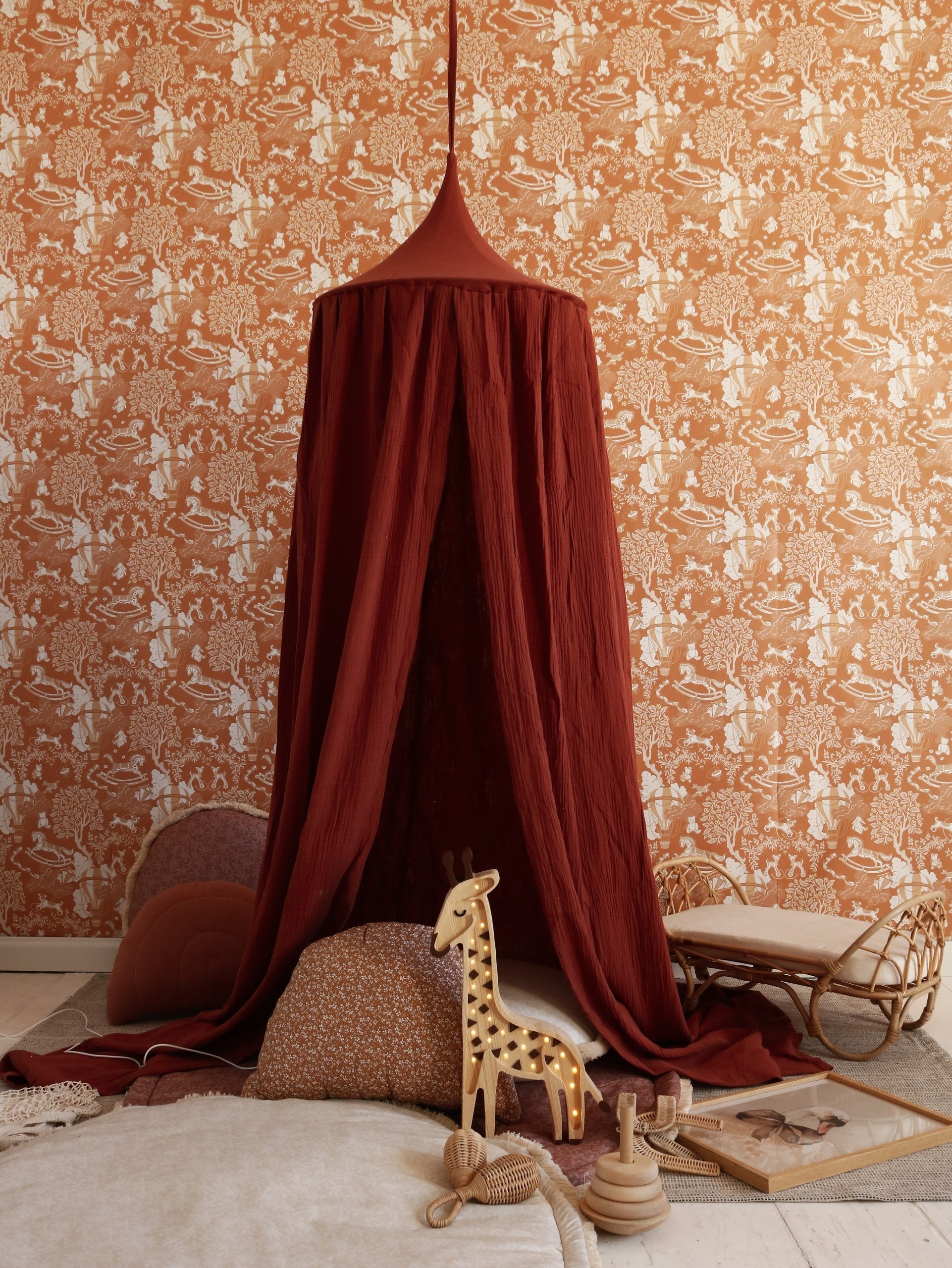 Yellow giraffe lamp glowing inside burgundy canopy tent in styled bedroom setup