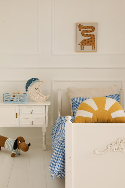 Moon lamp with LED lights glowing on white nightstand next to child's bed with checkered bedding