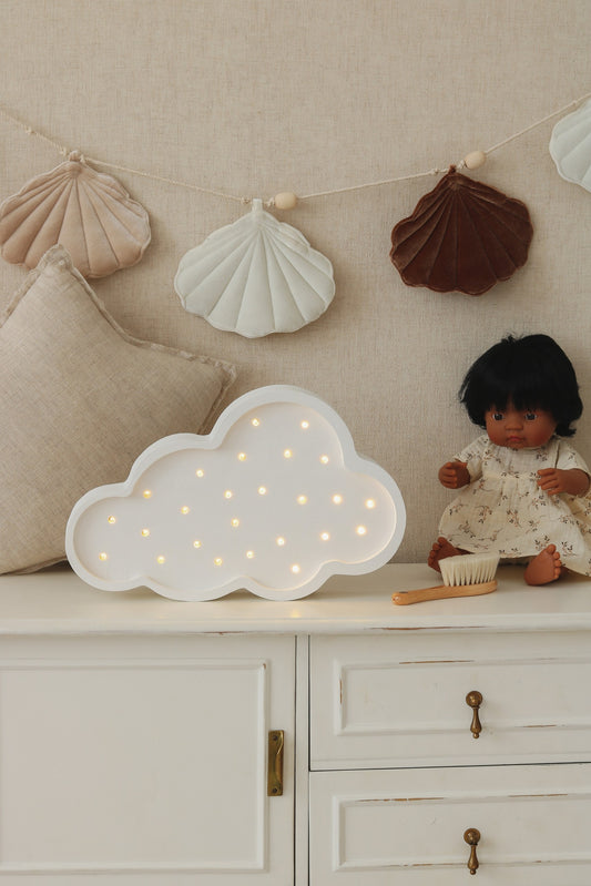 White cloud lamp with warm LED lights on nursery dresser next to decorative shell garland