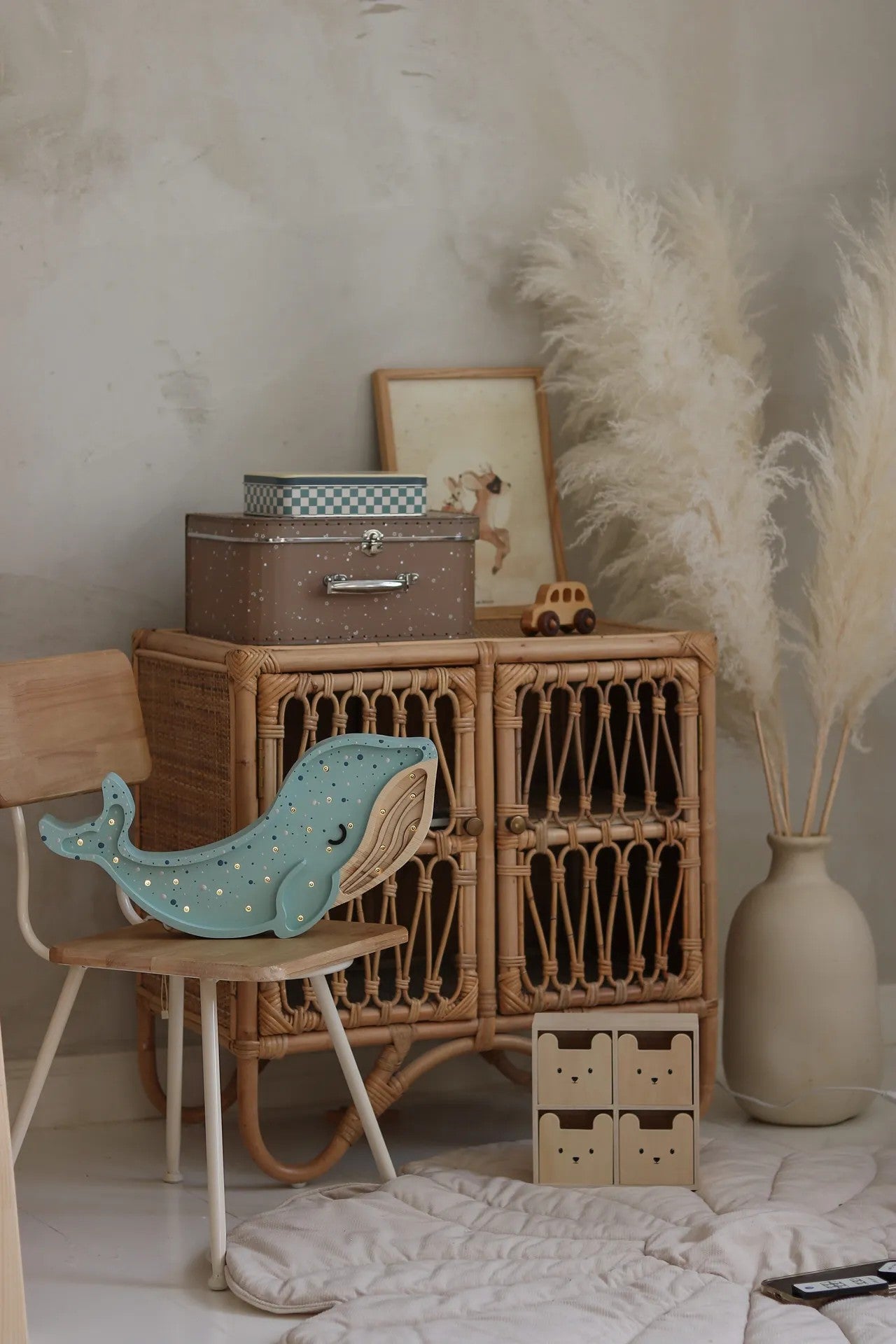 Cream colored whale lamp styled on wooden shelf with books, dried pampas and home decor items