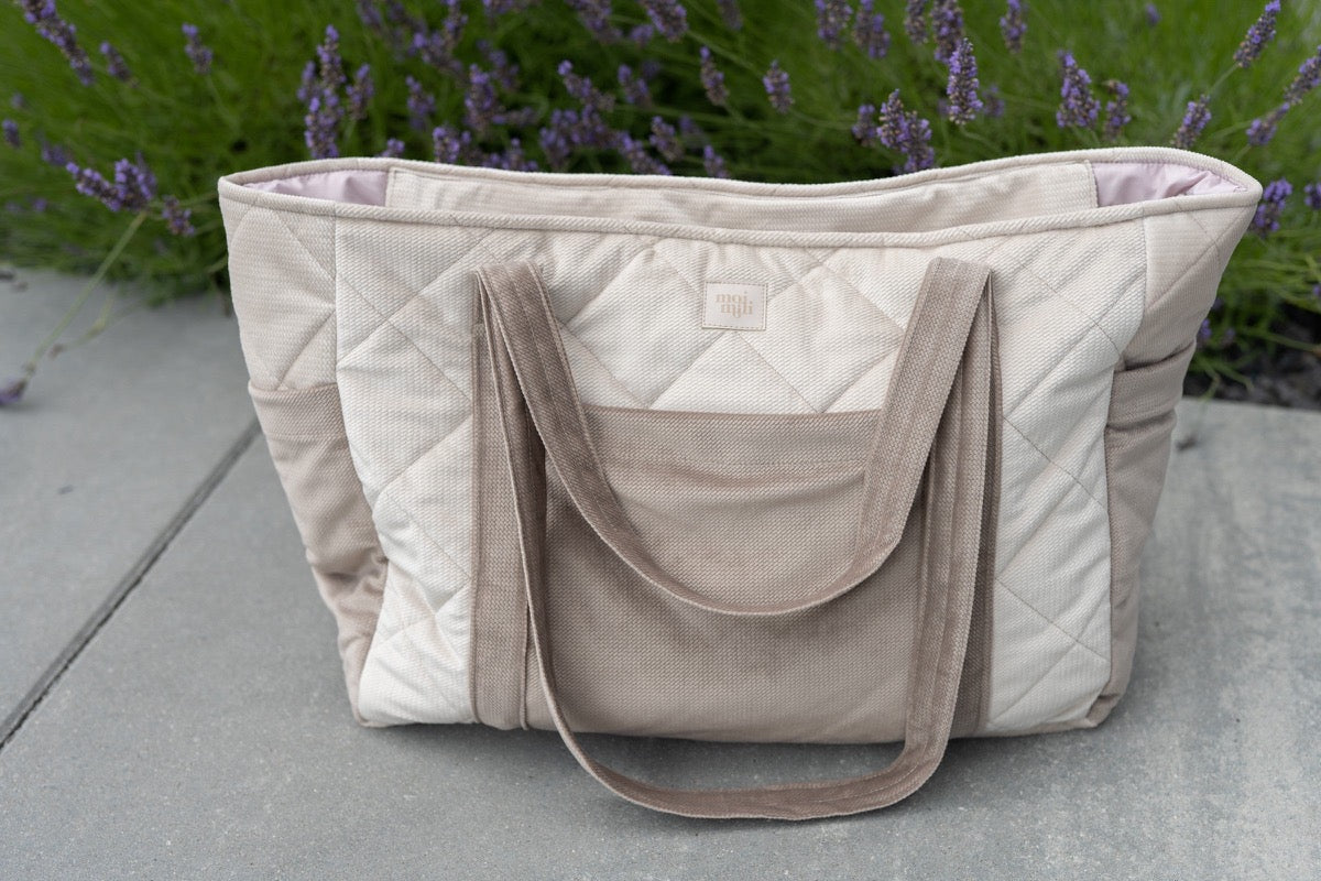 Beige quilted velvet weekender bag shown from above next to purple lavender plants outdoors