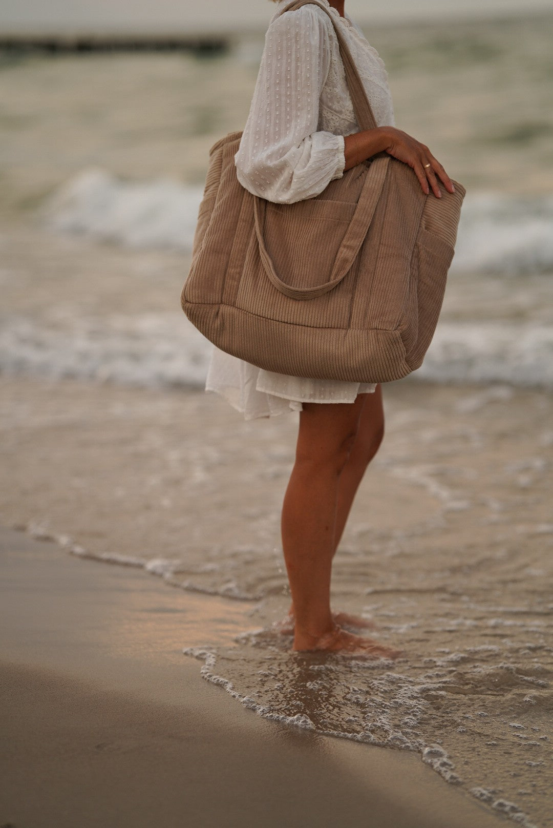 Woman carrying latte weekender bag over shoulder at ocean shore