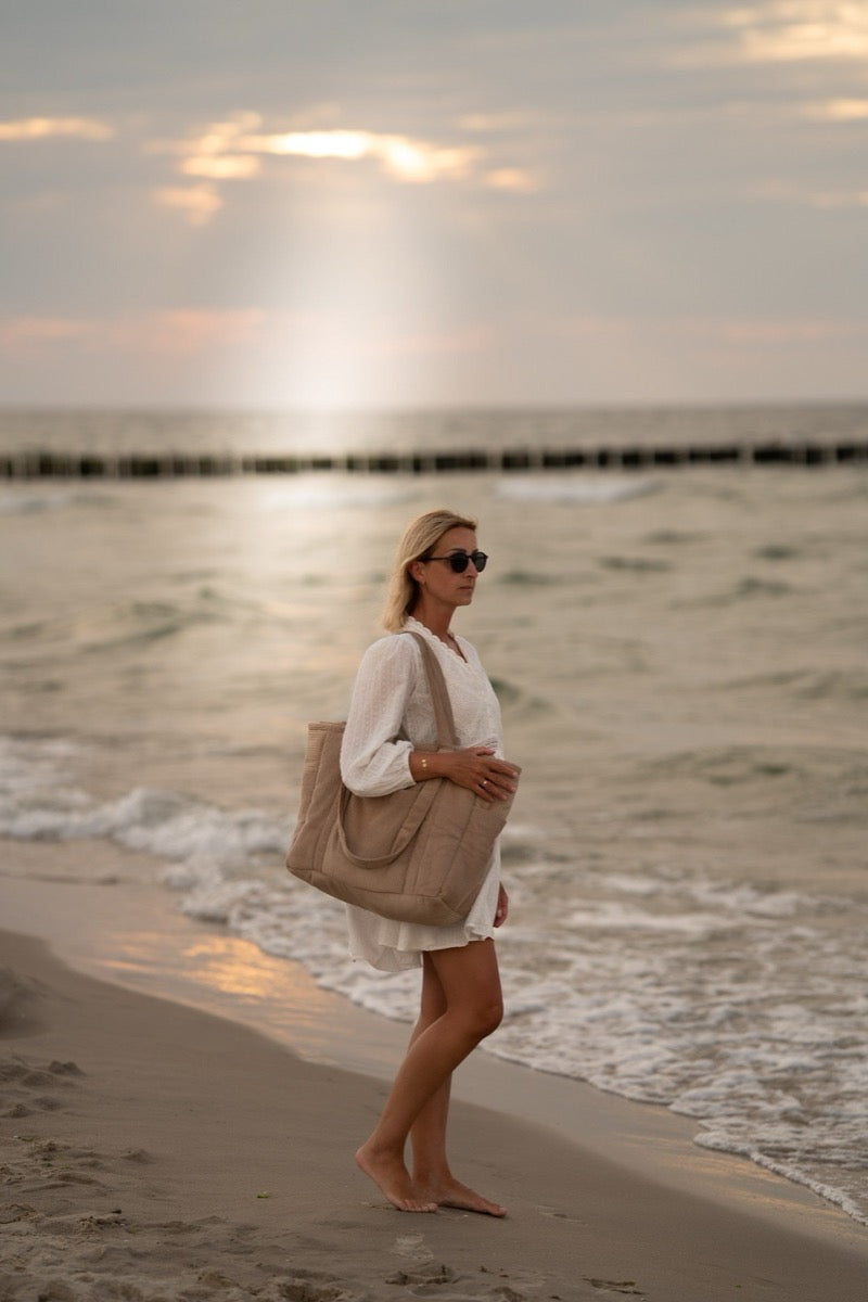 Woman wearing white walking along beach with latte velvet weekender bag
