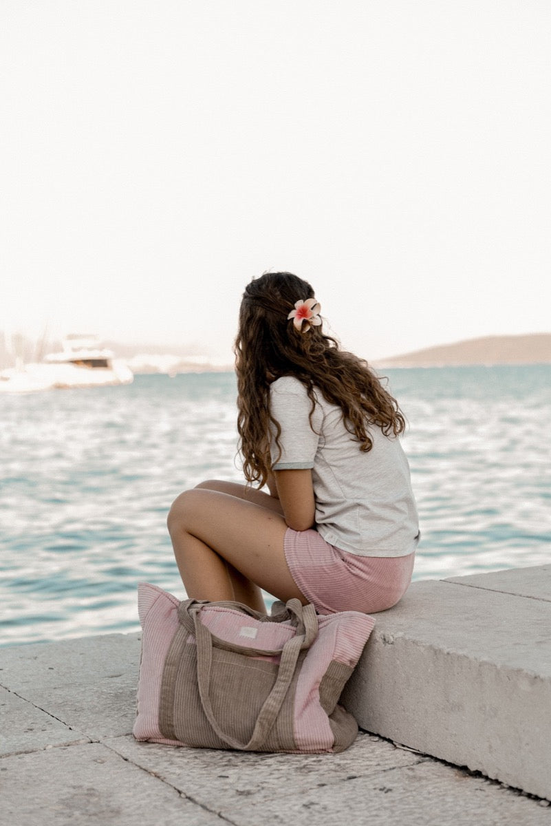 Woman by water with pink coffee weekender bag placed on ground