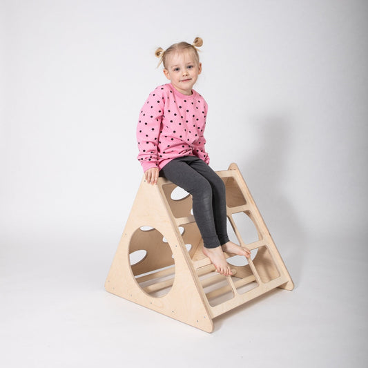 Toddler sitting on top of wooden climbing triangle with cutout handles
