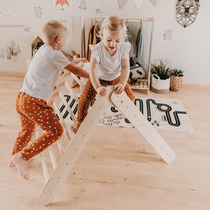 Two young children climbing on wooden triangle in Montessori-style playroom