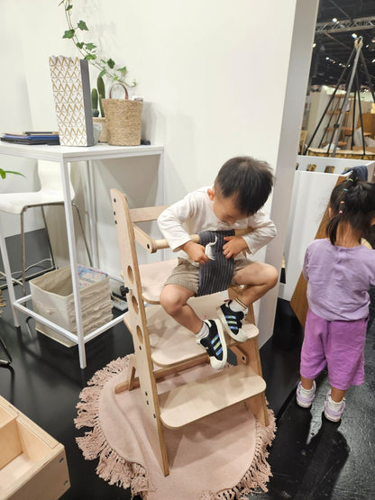 Toddler standing on wooden learning tower platform at kitchen counter during play activity