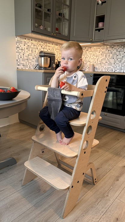 Young child seated in adjustable learning tower high chair at kitchen dining area