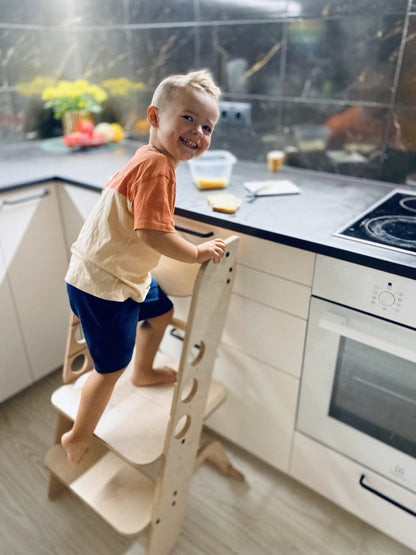 Toddler using learning tower as kitchen helper stool to reach counter height