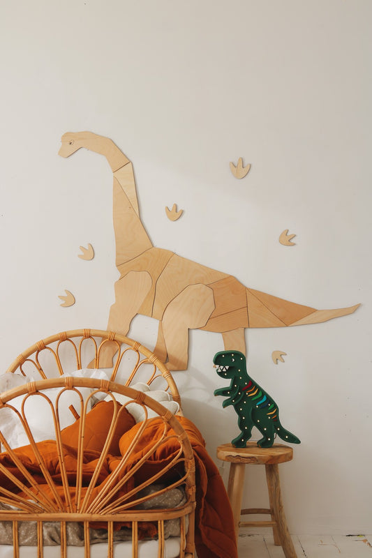 Wooden wall-mounted diplodocus with origami-style segments and small footprint decorations on white wall