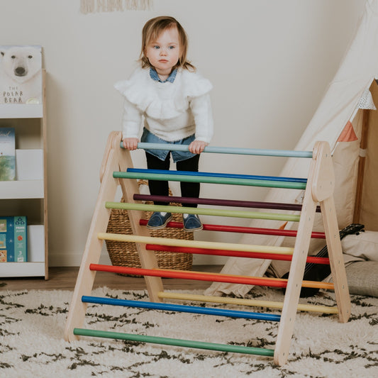 Toddler climbing and pulling up on rainbow-colored wooden bars of leg&go Pikler Triangle in bedroom