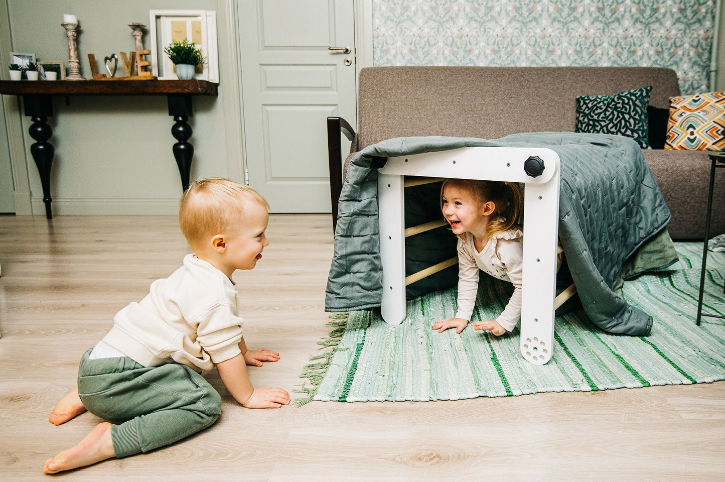 Child crawling under white Pikler triangle tunnel configuration in bedroom setting