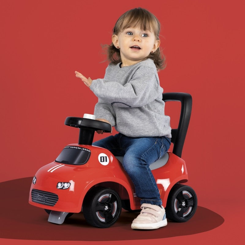 Toddler sitting on red Smoby ride-on car with handle, outdoor play demonstration