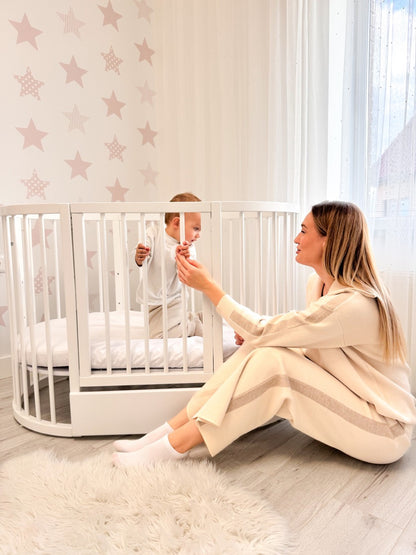 Woman sitting beside white round crib playing with toddler in star-themed nursery room