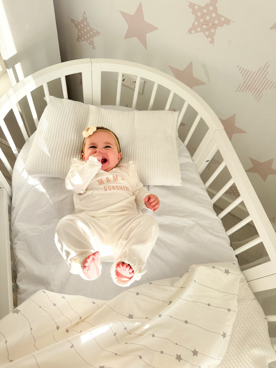 Newborn sleeping peacefully in round wooden crib with white bedding