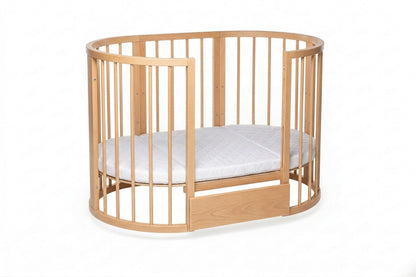 Natural wood oval crib with white mattress and adjustable base height