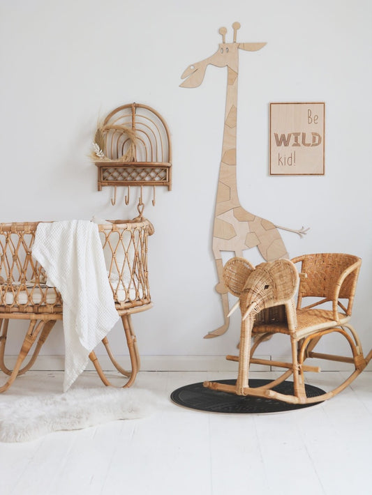 Wooden safari giraffe wall decoration displayed in neutral nursery with wicker furniture and safari-themed decor