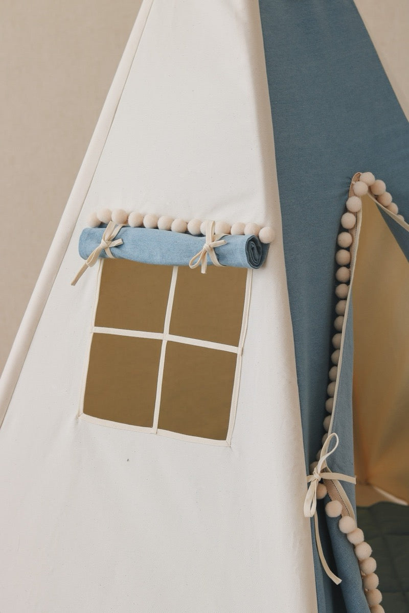 Close-up of teepee window detail showing pom pom trim and wooden curtain rod with blue fabric