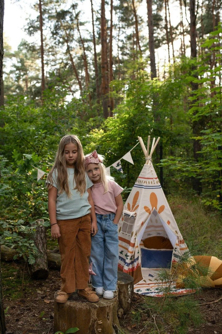 Two children standing outside in forest next to assembled Native Vibe teepee tent with orange and navy geometric patterns