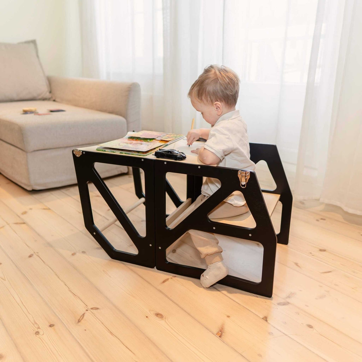 Toddler sitting at black transformable kitchen tower folded into table and chair set