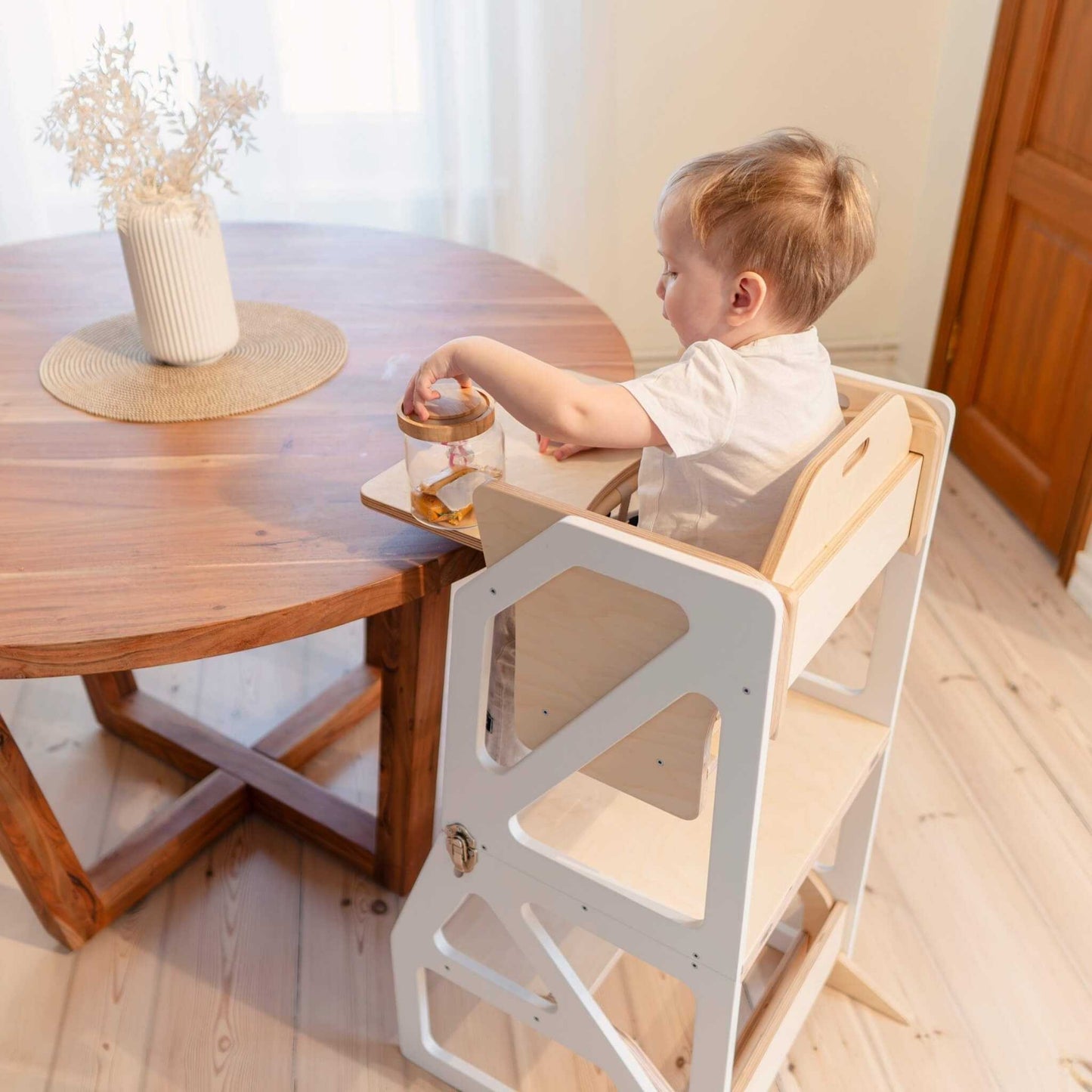 Toddler sitting at dining table on natural wood Modustep high chair with tray