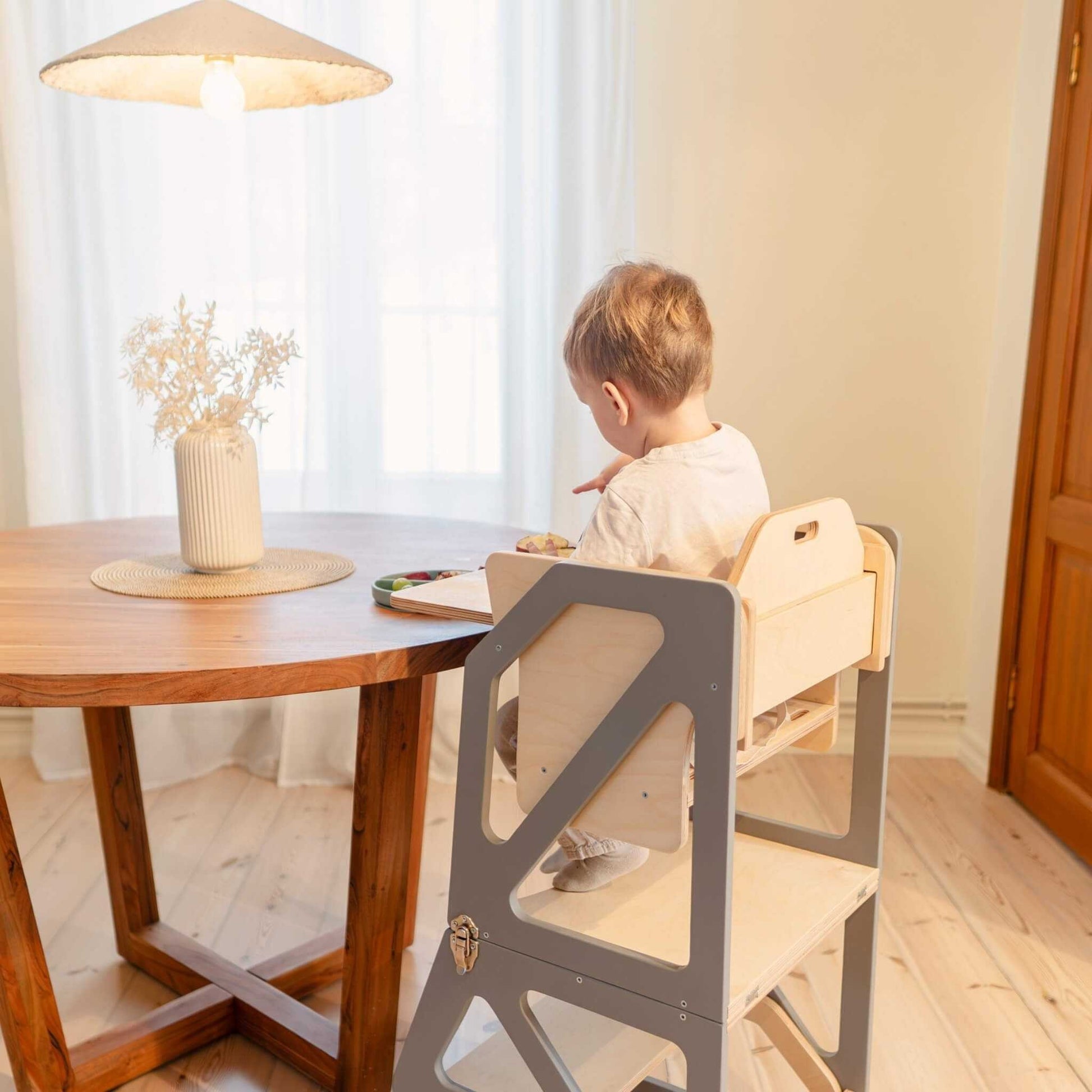 Toddler seated at dinner table in gray Modustep chair with wooden tabletop