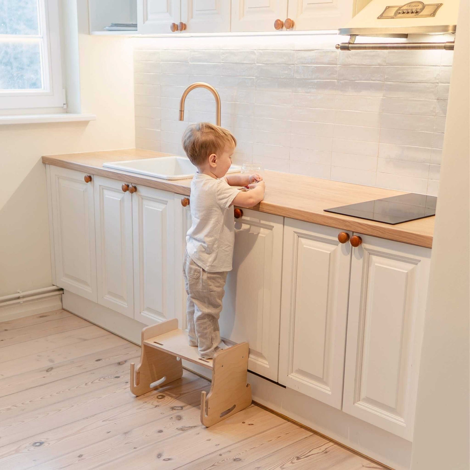 Young child reaching kitchen countertop with natural wood kitchen tower step