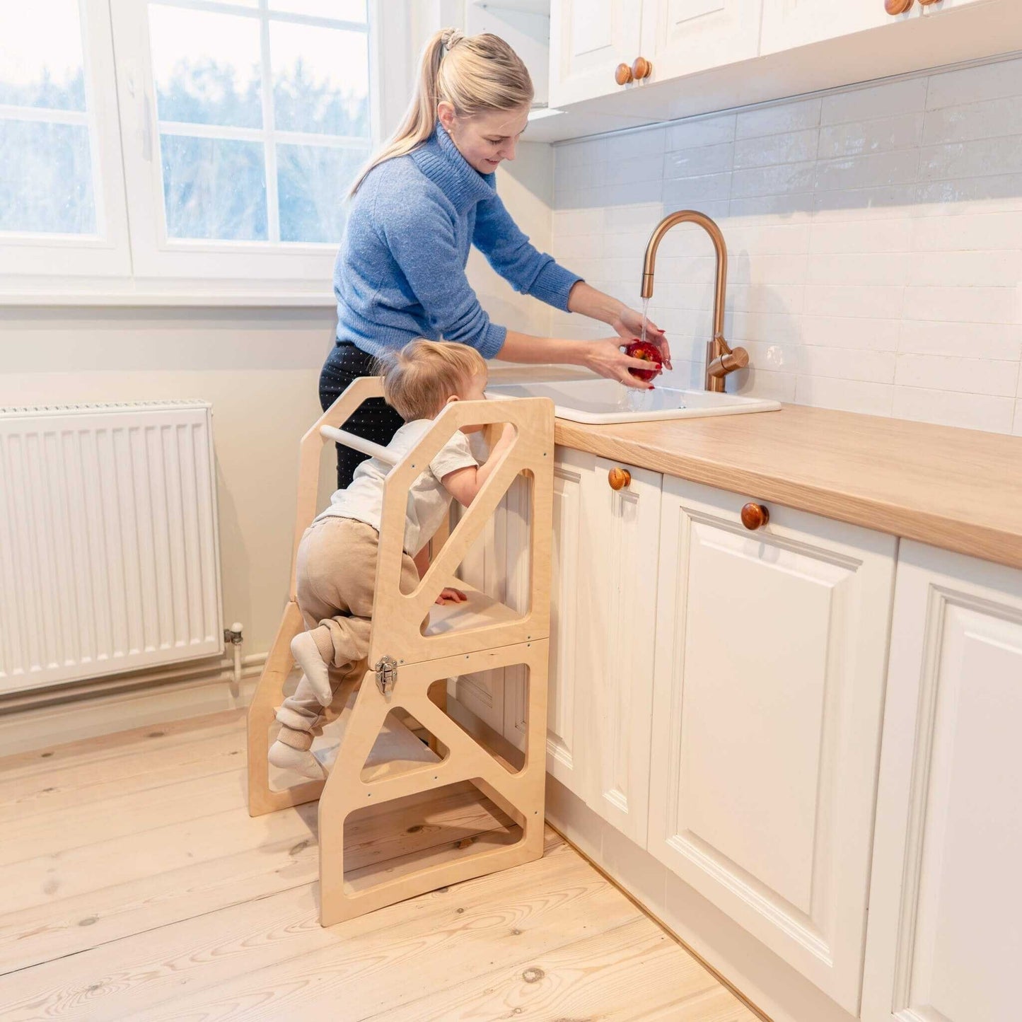 Adult supervising toddler using natural wood kitchen tower at kitchen sink