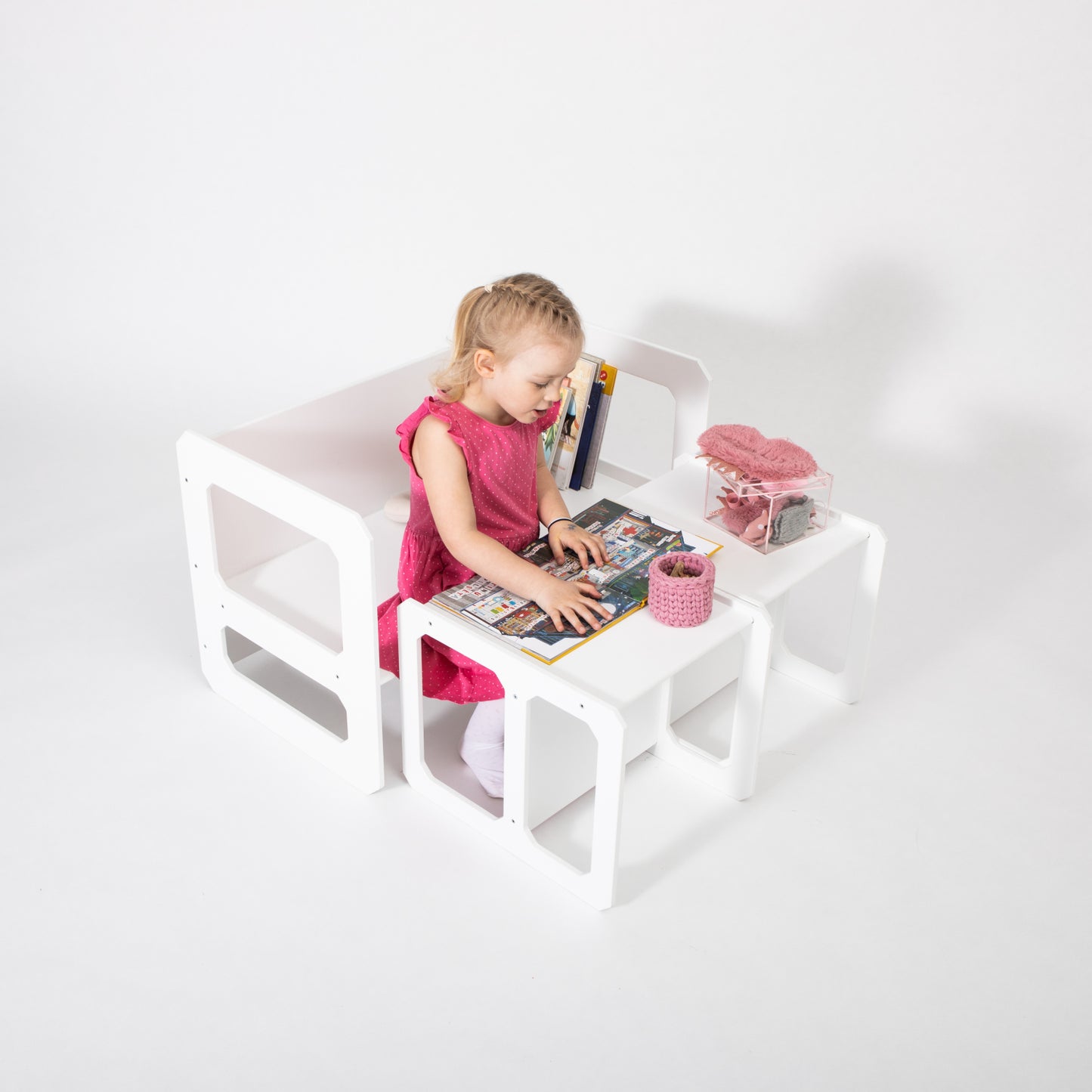 Toddler in pink dress sitting at white Montessori weaning table with matching chair, playing with toys