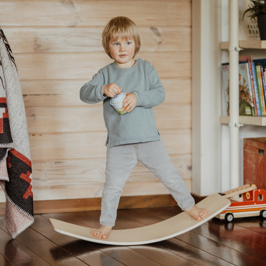 Toddler balancing on wooden board with arms out, developing coordination and motor skills